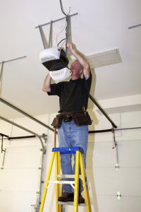 Man Standing on Ladder Servicing Garage Door Opener
