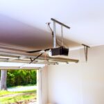 Black garage door opener motor unit mounted on a garage ceiling, with the door open to a sunny yard