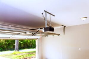 Black garage door opener motor unit mounted on a garage ceiling, with the door open to a sunny yard